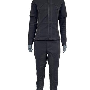 May include: A black two-piece outfit consisting of a long-sleeved jacket with a high collar and matching trousers. The jacket features a front placket, structured seams, and horizontal stitching on the sleeves. The trousers have vertical seams.