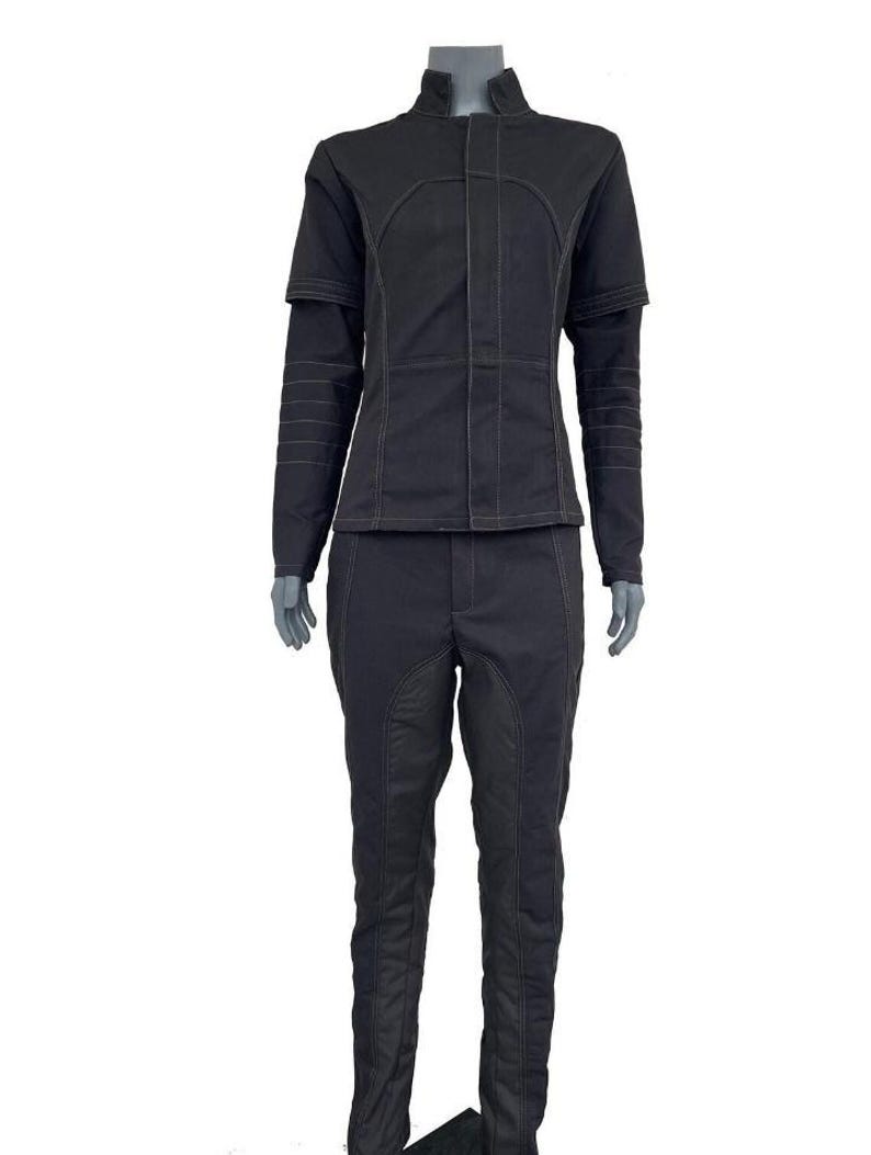 May include: A black two-piece outfit consisting of a long-sleeved jacket with a high collar and matching trousers. The jacket features a front placket, structured seams, and horizontal stitching on the sleeves. The trousers have vertical seams.