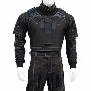 K&ouml;nnte beinhalten: Schwarzes taktisches Outfit mit wei&szlig;en Steppn&auml;hten. Das Outfit besteht aus einem hochgeschlossenen Oberteil mit Schulterakzenten und kurzem Bund, kombiniert mit einer passenden Hose. Das Design hat mehrere quadratische Patches und einen G&uuml;rtel.