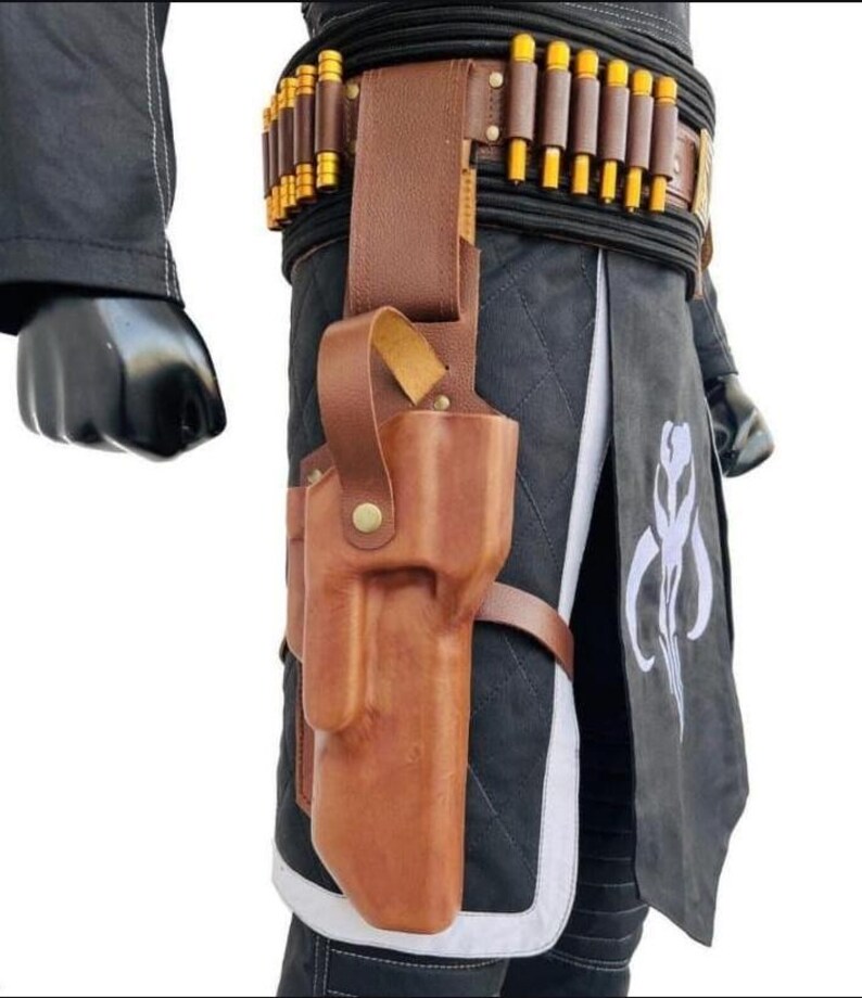 May include: A brown leather holster with a matching belt and cartridge holders. The holster is attached to a black and gray outfit with a white emblem. The belt features gold-colored cylindrical accents.