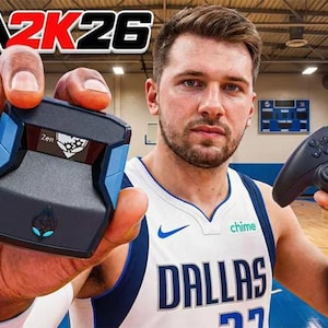 Puede incluir: Un hombre sostiene un mando de juegos negro y un dispositivo de juego negro y azul. El texto "NBA2K26" está en la parte superior. El hombre lleva una camiseta de los Dallas Mavericks.