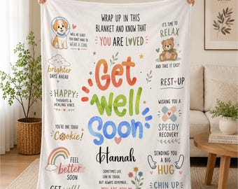 May include: A white fleece blanket featuring the text Get Well Soon and the name Hannah in black script. The design includes colorful illustrations of a puppy, a teddy bear, a rainbow, flowers, and encouraging phrases like You Are Loved.