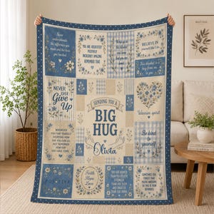 May include: A rectangular throw blanket featuring a patchwork design in shades of blue, white, and beige. The blanket displays various inspirational quotes, floral illustrations, and the central text, "Sending you a big hug, Olivia," with a graphic of arms.