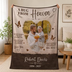 May include: A beige and brown fleece blanket featuring a central heart-shaped photo of a person holding a child. Text reads A HUG FROM HEAVEN, EVEN WHEN I'M NOT CLOSE BY, I WANT YOU TO KNOW I ALWAYS LOVE YOU, WRAP YOURSELF UP IN THIS AND CONSIDER IT A BIG HUG, Robert Davis, 1950-2025, with butterfly and heart graphics.