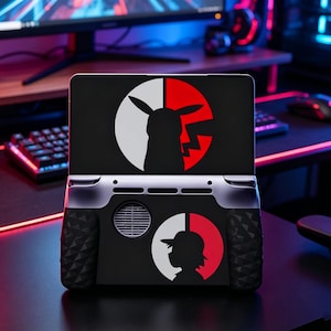 Puede incluir: Un dispositivo de juego portátil negro y plateado con un diseño de silueta de Pikachu y entrenador. El dispositivo tiene una pantalla negra con un gráfico rojo y blanco. El fondo incluye un teclado, un ratón y un monitor.