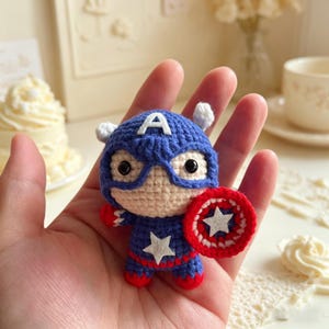 Hand holding a small handmade crochet star shield hero amigurumi doll with big eyes and blue suit in a cozy cream colored room