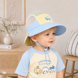 May include: A multi-colored sun hat featuring a light blue brim, a pale yellow front panel with a small blue car graphic, and white mesh side panels. The hat includes a chin strap with an adjustable toggle and a yellow neck flap for sun protection.