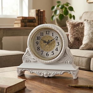 May include: A white, ornate mantel clock with a gold-colored clock face. The clock features Roman numerals and decorative hands. The clock is set on a white base with a scrolled design. The clock is approximately 8 inches tall.