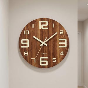 Puede incluir: Reloj de pared redondo de madera con acabado de vetas de madera marrón. El reloj presenta grandes números y manecillas blancos iluminados. La palabra "QUARTZ" está impresa en la parte inferior. Un diseño moderno y minimalista para la decoración del hogar.