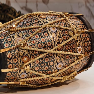 Op de afbeelding: Een sierlijke trommel met een patroon van bloemen in rood, goud en wit op een donkere achtergrond. De trommel heeft zwarte randen en gouden touwen en metalen details. Het is een decoratief muziekinstrument.