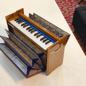 May include: A brown and gold harmonium with a keyboard and bellows. The instrument has a blue accent and decorative patterned panels. The keys are black and white. The harmonium is a musical instrument.