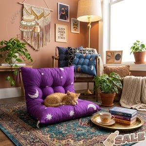 May include: A cozy interior scene featuring a purple floor cushion with a celestial design, including moons and stars. An orange cat is curled up on the cushion. The room is decorated with plants, pillows, and artwork, creating a relaxing atmosphere.