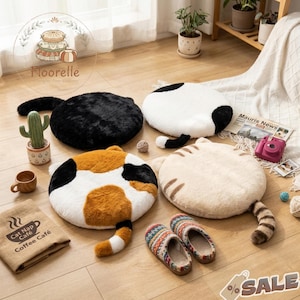 Puede incluir: Cuatro cojines de suelo con forma de gato en colores negro, blanco, calicó y crema, cada uno con cola. También se ven un par de zapatillas estampadas, un cactus y una bolsa de café. Los cojines están diseñados para parecer gatos.