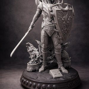 Peut inclure: Figurine grise détaillée d'un chevalier en armure complète, tenant une épée et un bouclier. Le bouclier présente un motif de dragon. Le chevalier se tient sur une base ronde avec des éléments décoratifs et le texte "ATK3000".