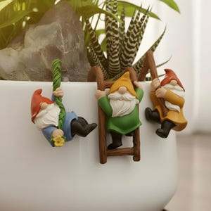 Könnte beinhalten: Ein Set aus drei Keramikbechern mit gesprenkelter, matter Oberfläche. Die Becher sind in Creme-, Hellgrau- und Dunkelgrautönen gehalten. Jeder Becher hat ein schlichtes, modernes Design und einen abgerundeten Henkel.