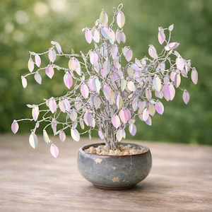 Könnte beinhalten: Ein dekorativer Bonsai-Baum mit silbernem Drahtstamm und Ästen, verziert mit schillernden, pastellfarbenen Blättern. Der Baum steht in einem kleinen, runden, blau-grauen Keramiktopf. Der Hintergrund ist ein weiches, verschwommenes Grün.