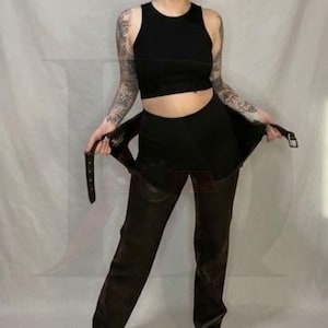 May include: A black sleeveless crop top paired with black trousers featuring an integrated belt with a silver buckle. The trousers have a high-waisted design and a straight-leg cut, with the belt ends held outward to display the hardware.