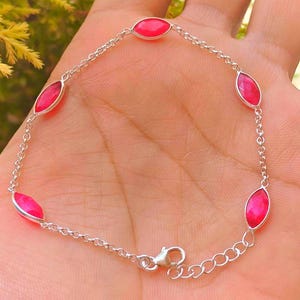 Puede incluir: Una pulsera de cadena plateada con cinco piedras de color rosa vibrante en talla marquesa, engastadas en biseles de metal pulido. La pulsera incluye una cadena de eslabones finos, un cierre de mosquetón y una cadena de extensión ajustable.
