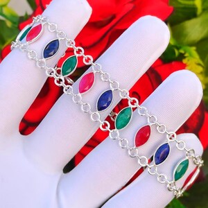 Puede incluir: Una pulsera de cadena de plata con un patrón repetitivo de piedras preciosas de corte marquesa en rojo vibrante, azul profundo y verde esmeralda. Las piedras están engastadas en marcos de plata pulida y unidas por delicados eslabones circulares.