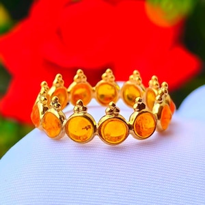 May include: A gold ring featuring a continuous band of circular, translucent orange stones set in polished gold bezels. Each stone setting is topped with a small, three-pronged decorative element, creating a crown-like appearance around the band.