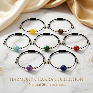 Può includere: Una collezione di sette braccialetti regolabili con cordini neri e dettagli dorati. Ogni braccialetto presenta una perla di pietra naturale di colore diverso: giallo, marrone, turchese, verde, rosso, viola e blu. Il testo "HARMONY CHAKRA COLLECTION Natural Stone & Beads" è sotto.