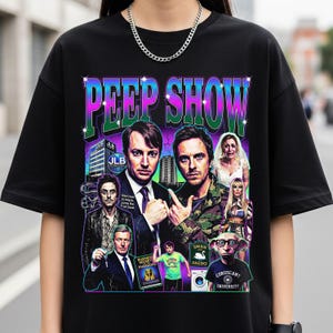 May include: Black t-shirt featuring a colorful graphic design with the text "PEEP SHOW" in a retro style. The design includes images of characters from the show. A silver chain necklace is visible.