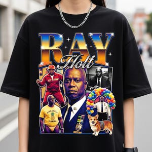 May include: Black t-shirt featuring a graphic of the name "Ray Holt" in a retro style. The design includes images of a man in various poses, a corgi, and the text "HOT DAMN!" and "Pineapple Florida".