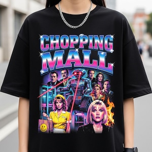 May include: Black t-shirt featuring a retro graphic design with the text "CHOPPING MALL" in a vibrant, multi-colored font. The design includes images of people and a robot, with a shopping bag with a smiley face.