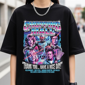 May include: Black t-shirt featuring a colorful graphic from the movie "Shopping Mall." The design includes the movie title, character illustrations, and the phrase "THANK YOU... HAVE A NICE DAY!"