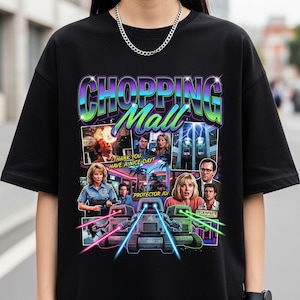 May include: Black t-shirt featuring a colorful graphic from the movie "Chopping Mall." The design includes the text "CHOPPING Mall" in a gradient font, along with images of characters and robots. The text "THANK YOU. HAVE A NICE DAY!" is also visible.