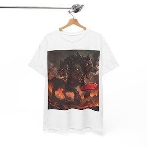 Peut inclure: T-shirt blanc avec un motif d'un loup noir à trois têtes aux yeux rouges, sur fond de feu et de fumée. Le loup tient un frisbee rouge. Le t-shirt est suspendu à un cintre en bois.