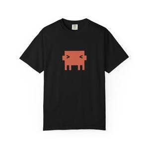 Op de afbeelding: Zwart T-shirt met een oranje geometrisch ontwerp. Het ontwerp is een gepixelde figuur met een rechthoekig lichaam, twee paar benen en armen. Het shirt heeft korte mouwen en een ronde hals. Eenvoudig, modern ontwerp.