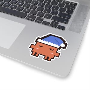 May include: A pixel art sticker featuring a small, orange, blocky character with a simple face and a blue nightcap with a white trim. The character has a rectangular body, two small arms, and two legs, all rendered in a distinct 8-bit style.