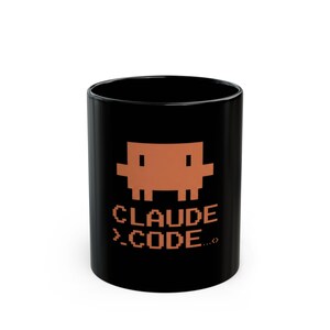 Peut inclure: Mug en céramique noire avec un personnage marron pixélisé et le texte "CLAUDE >.CODE...". Le mug a une finition brillante et une forme cylindrique. Le design rappelle les jeux vidéo rétro.
