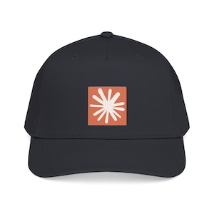 Op de afbeelding: Een donkergrijze honkbalpet met een gecentreerde vierkante patch. De patch is effen terracotta oranje van kleur met een wit, stervormig of zonachtig grafisch ontwerp met meerdere punten in het midden van het vierkant.