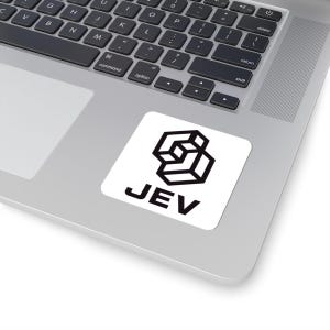 Puede incluir: Una pegatina cuadrada blanca con un logotipo geométrico negro compuesto por cubos interconectados y el texto JEV en una fuente sans-serif en negrita. La pegatina está aplicada sobre la superficie metálica plateada de un ordenador portátil.