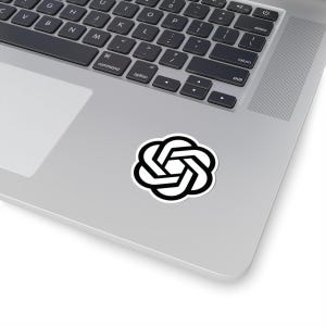 Puede incluir: Una pegatina blanca con un diseño geométrico en blanco y negro, que se asemeja a una flor o nudo estilizado, está colocada sobre un portátil plateado. El diseño de la pegatina es una serie de formas interconectadas, creando un patrón simétrico.