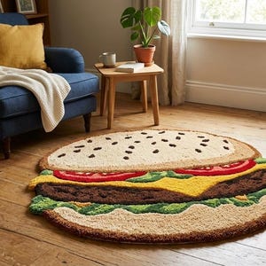 May include: A round rug shaped like a hamburger, featuring a beige bun, a brown patty, yellow cheese, red tomato slices, and green lettuce. The rug is placed on a wooden floor in a room with a blue armchair and a side table.