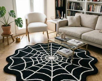May include: A black and white spiderweb-shaped rug with a scalloped edge. The rug is placed on a hardwood floor in a living room setting, with a couch, chair, and coffee table visible in the background.