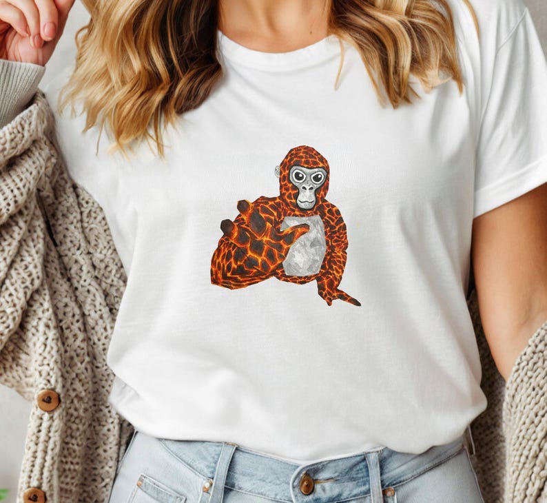 May include: White t-shirt featuring a cartoon orangutan design. The orangutan has a textured orange and black pattern on its body and a light gray chest. The design is centered on the front of the shirt.