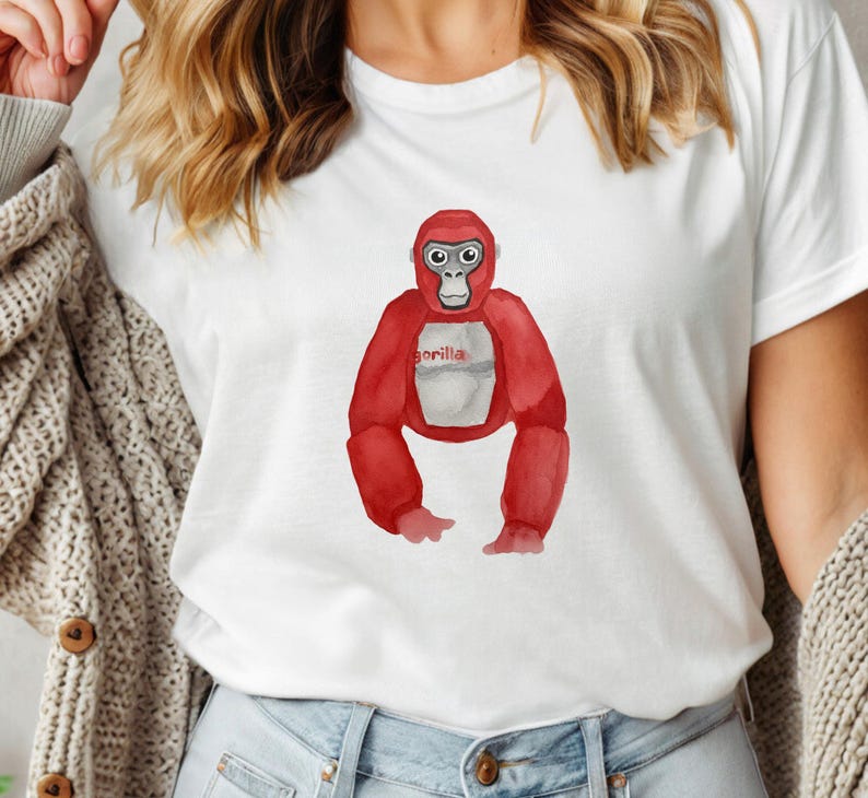 May include: White t-shirt featuring a red watercolor gorilla illustration. The gorilla has a white belly and the word "gorilla" printed on it. The shirt is made of a soft material.