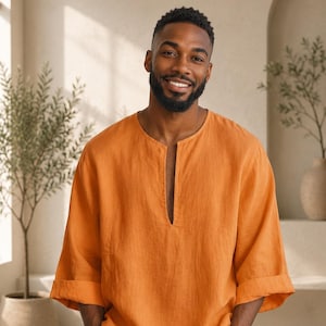 May include: An orange linen shirt with a V-neck and rolled-up sleeves. The shirt is part of a fashion collection, as indicated by the "AA - FASHION FORWARD" text in the lower right corner. The model is smiling.