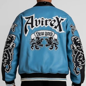 Peut inclure: Veste en cuir bleu clair avec des d&eacute;tails noirs et blancs. Le dos affiche le texte "Avirex New York" et des embl&egrave;mes de lion. Col et poignets noirs, ourlet ray&eacute; noir, blanc et bleu clair.
