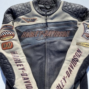 Può includere: Una giacca da moto Harley-Davidson nera, beige e grigia. La giacca presenta il logo Harley-Davidson sul petto e sulle maniche. Le toppe sulle maniche e sul petto includono le parole "American Legend" e "Harley-Davidson Motorcycles".