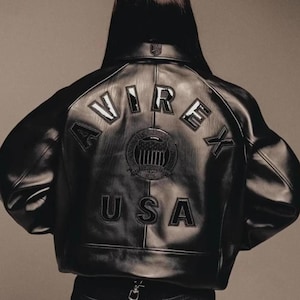 May include: Black leather jacket with the word "AVIREX" arched across the back, above a circular emblem and the word "USA". The jacket has a classic bomber style with a ribbed collar and cuffs.