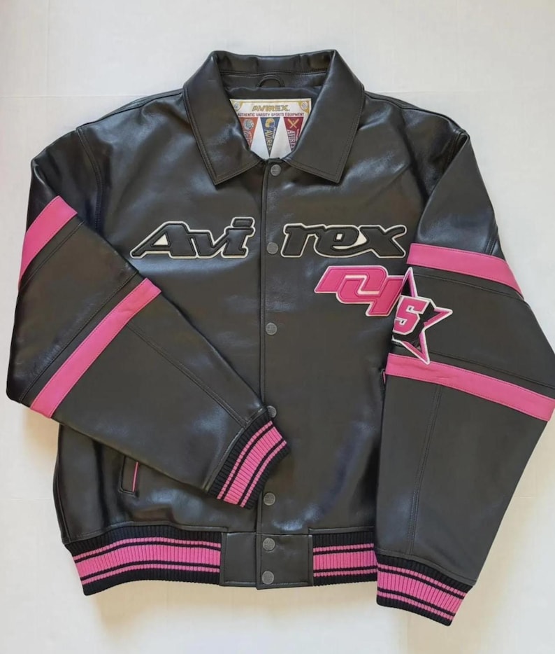 Puede incluir: Chaqueta de cuero negra con detalles rosas y el logo de Avirex. La chaqueta tiene cierre de botones, pu&ntilde;os y dobladillo acanalados con rayas rosas y negras, y una estrella en la manga. Las mangas tienen rayas rosas.
