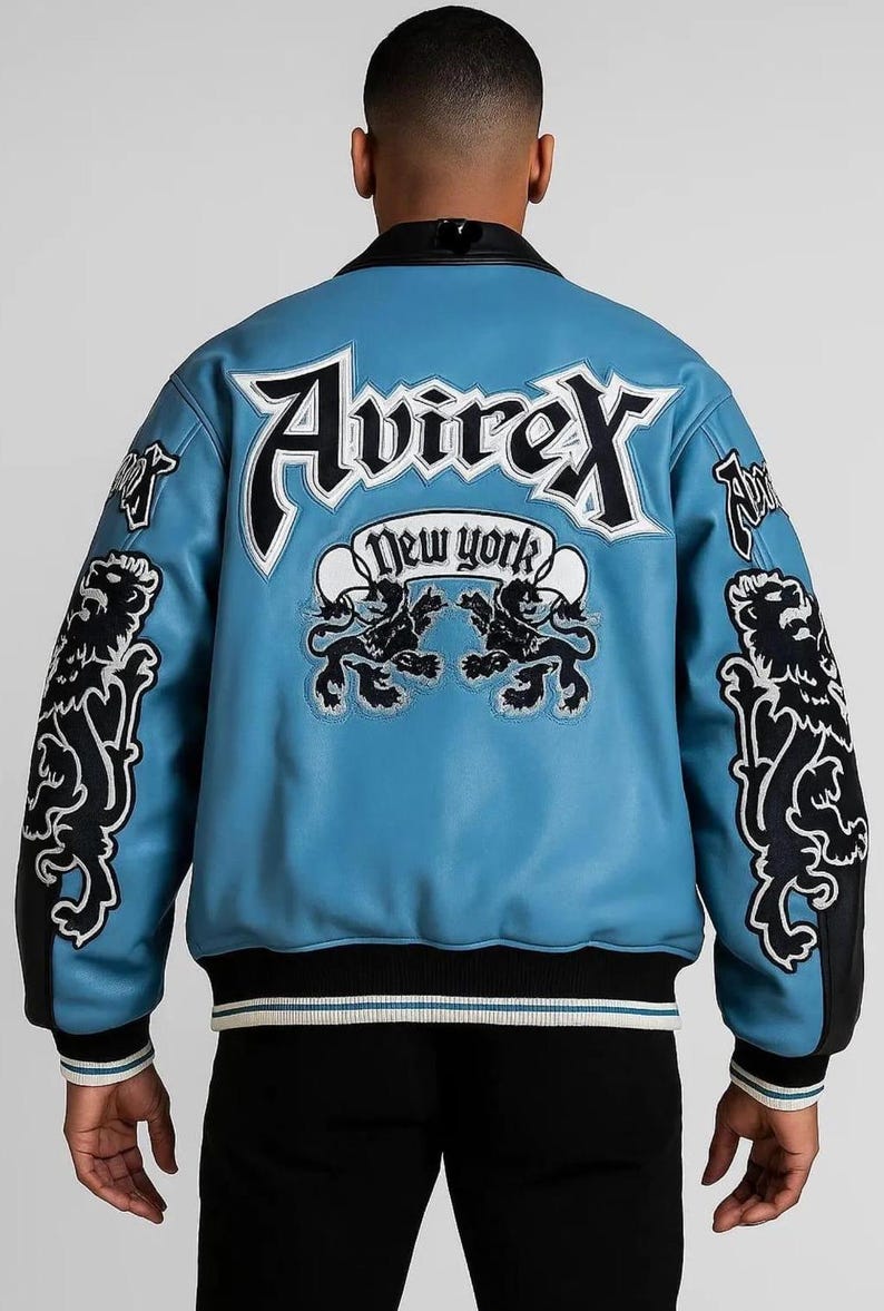Peut inclure: Veste en cuir bleu clair avec des d&eacute;tails noirs et blancs. Le dos affiche le texte "Avirex New York" et des embl&egrave;mes de lion. Col et poignets noirs, ourlet ray&eacute; noir, blanc et bleu clair.