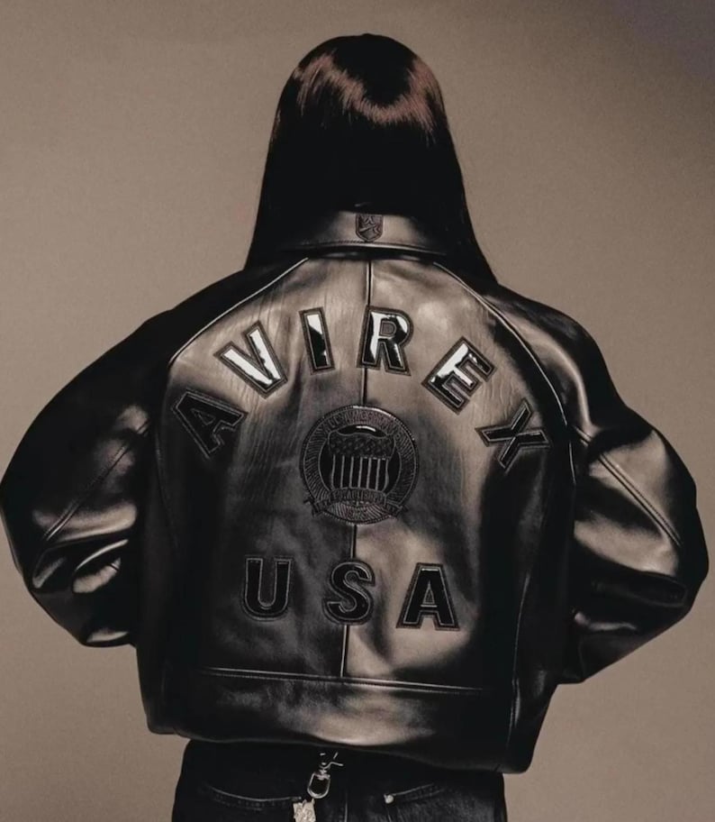 May include: Black leather jacket with the word "AVIREX" arched across the back, above a circular emblem and the word "USA". The jacket has a classic bomber style with a ribbed collar and cuffs.