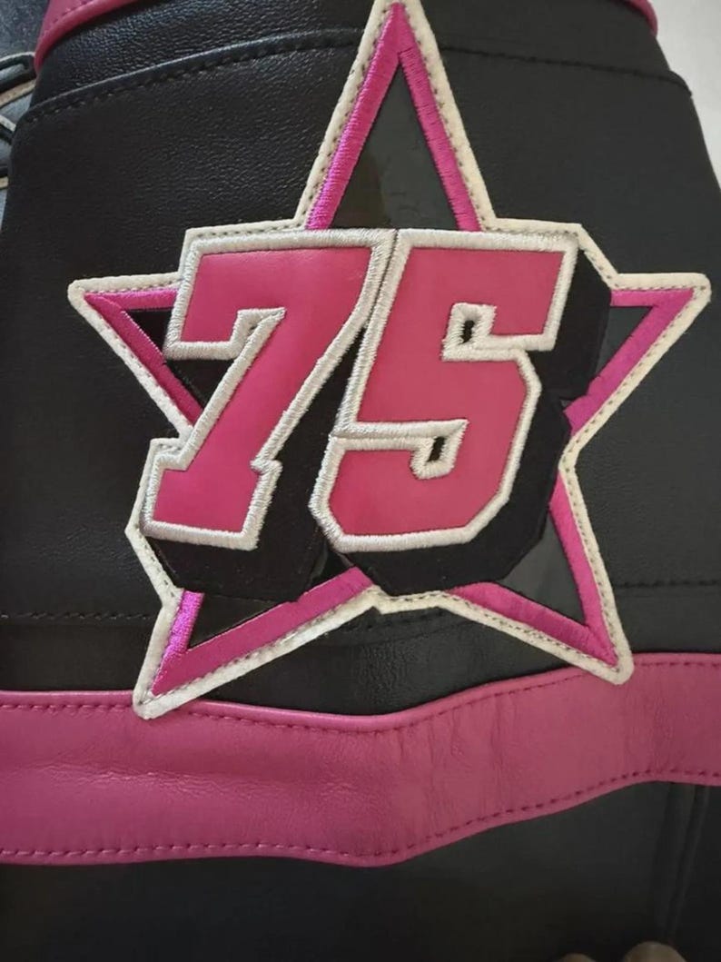 Puede incluir: Detalle de una chaqueta de cuero negra con un parche de estrella rosa con el n&uacute;mero 75. El parche tiene un contorno blanco y est&aacute; cosido a la chaqueta. Una franja de cuero rosa recorre la parte inferior.