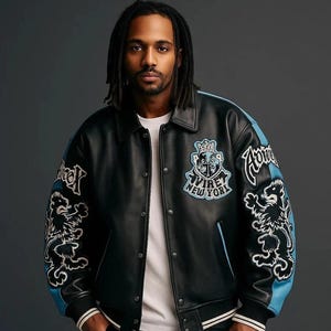 Peut inclure: Veste en cuir noire avec des d&eacute;tails et des &eacute;cussons bleus. La veste a une fermeture boutonn&eacute;e, un col et des &eacute;cussons avec du texte et un motif de lion. Le texte sur la veste dit "AVIRE NEW YORK".